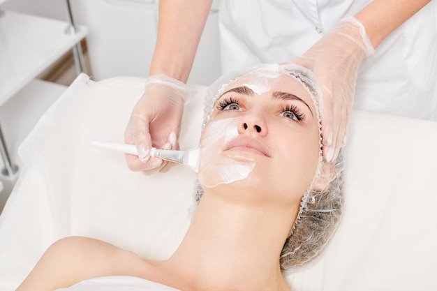 L'estetista applica la maschera crema sul viso della donna per la procedura di ringiovanimento della pelle del viso nel salone di bellezza