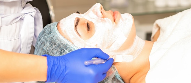 L'estetista con il pennello applica una maschera viso peeling fotochimica e glicolica sul viso della paziente nella clinica di bellezza