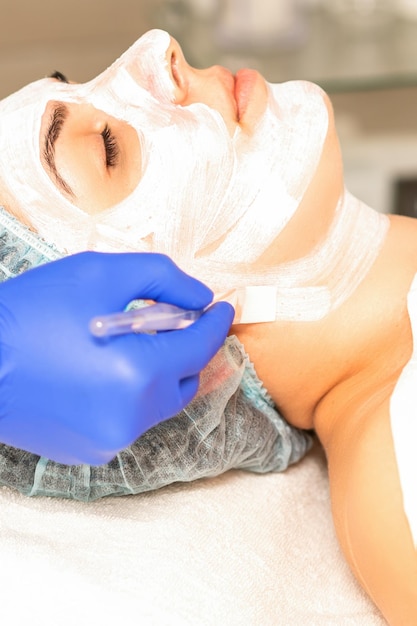 L'estetista con il pennello applica una maschera viso peeling fotochimica e glicolica sul viso della paziente nella clinica di bellezza