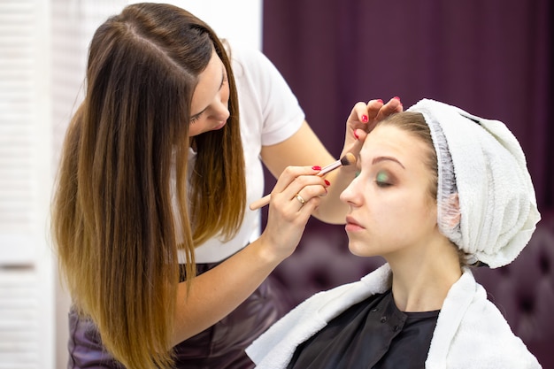 L'estetista dipinge le palpebre della giovane bella ragazza con il pennello cosmetico