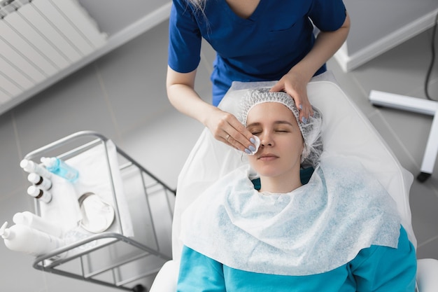L'estetista pulisce il viso del paziente con un batuffolo di cotone nel suo ufficio