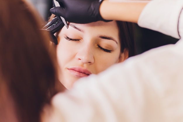 L'estetista-truccatrice applica l'henné di vernice su sopracciglia strappate, progettate, tagliate in un salone di bellezza nella correzione della sessione. Cura professionale per il viso.