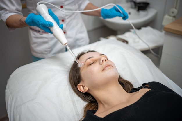 L'estetista utilizza il dispositivo darsonval sul viso del cliente Cura della pelle professionale nel salone Il concetto di cosmetologia e ringiovanimento