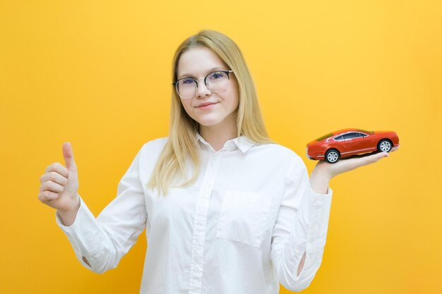 L'idea e il concetto di scuola guida studente conducente ha superato l'esame patente di guida ritratto di una bella giovane donna felice che tiene un'auto in mano su uno sfondo giallo guardando l'auto