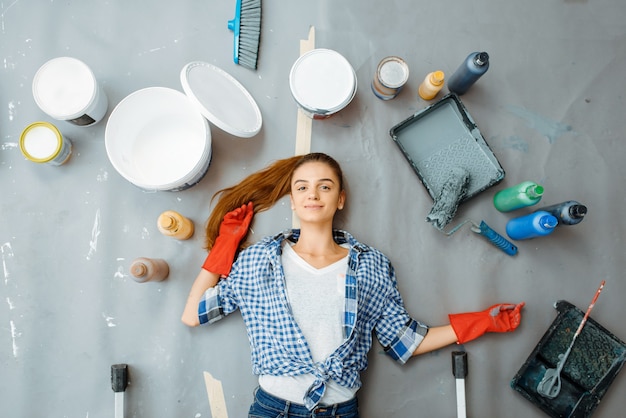 L'imbianchino femminile allegro si trova sul pavimento, vista dall'alto. Riparazione della casa, donna felice che fa ristrutturazione dell'appartamento, ristrutturazione della decorazione della stanza