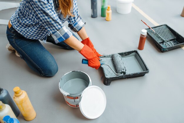 L'imbianchino femminile impregna il rullo di vernice. Riparazione della casa, donna ridente che fa lavori di ristrutturazione dell'appartamento, ristrutturazione della decorazione della stanza