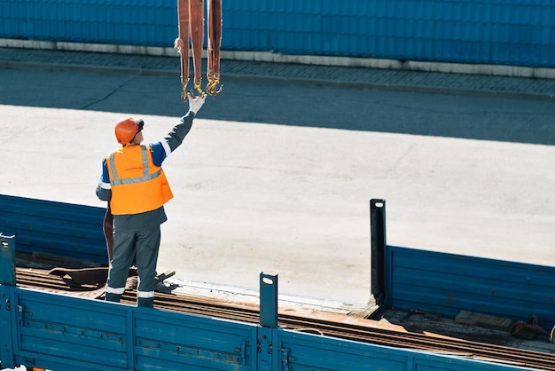 L'imbracatura in casco e giubbotto scarica tubi metallici e raccordi dal cassone del camion in una giornata limpida Contesto della produzione Autentico flusso di lavoro in cantiere Imbracatrice al lavoro