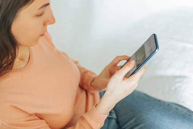 L'immagine autentica vista dall'alto mostra una giovane donna che naviga sul suo smartphone mentre è seduta sul suo divano a ho