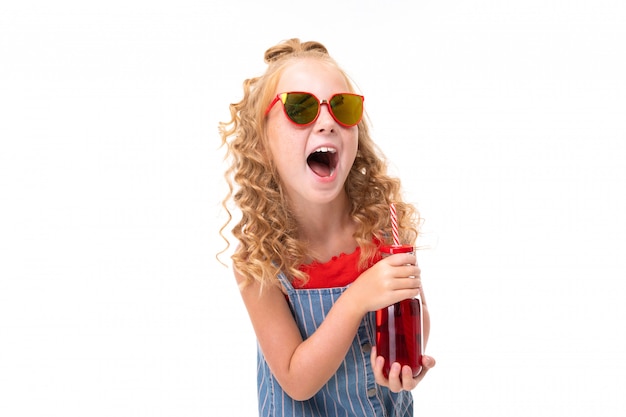 L'immagine del bambino felice con capelli ricci rossi giusti beve il succo e la risata rossi