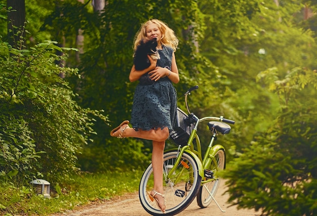 L'immagine del corpo intero della ragazza bionda tiene il cane Spitz su sfondo di bicicletta.