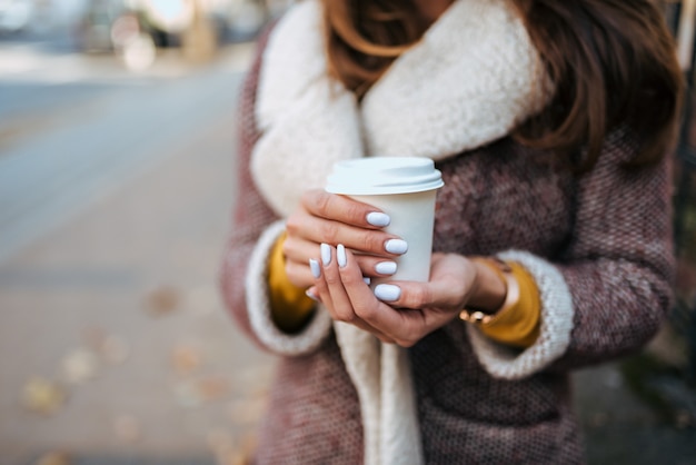 L&#39;immagine del primo piano della tenuta della giovane donna porta via la tazza di caffè all&#39;aperto.