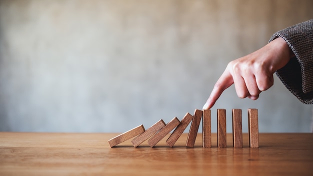 L'immagine del primo piano di un dito cerca di fermare la caduta di blocchi di domino in legno per il concetto di soluzione aziendale