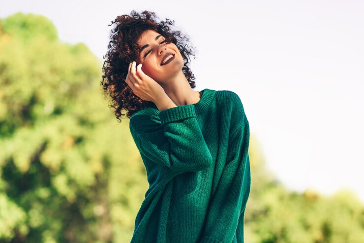 L'immagine della bella giovane donna felice che sorride in posa sullo sfondo della natura con i capelli ricci ventosi ha un'espressione positiva che indossa un maglione verde La gente viaggia e lo stile di vita