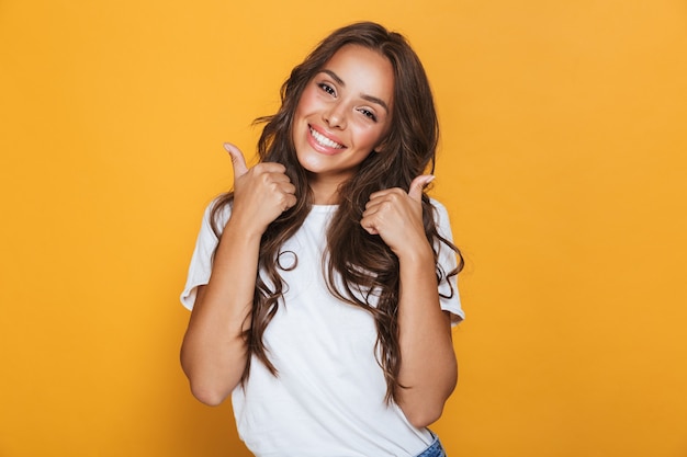 L'immagine della giovane donna felice isolata sopra la parete gialla che mostra i pollici aumenta il gesto.
