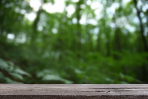 L'immagine della tavola di legno grigia davanti all'estratto ha offuscato il fondo delle foglie verdi e degli alberi