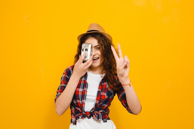 L'immagine di bella donna che prende una foto con una retro macchina fotografica e mostra i gesti isolati sopra la parete gialla