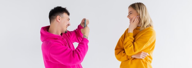 L'immagine di un uomo scatta una foto della sua donna ottimista positiva su sfondo bianco con il telefono cellulare