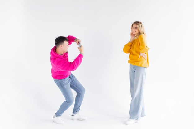 L'immagine di un uomo scatta una foto della sua donna ottimista positiva su sfondo bianco con il telefono cellulare