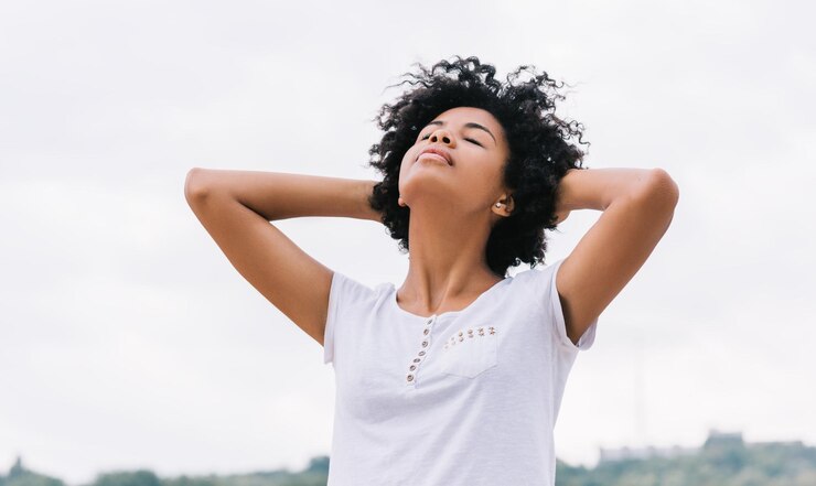 L'immagine di una donna afroamericana felice che riposa all'aperto nel parco con le mani sulla testa sollevata e gli occhi chiusi si sente libera Bella giovane donna dalla pelle scura godersi la natura e una vita sana Persone