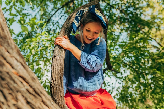 L'immagine di una giovane donna divertente si diverte sull'albero sullo sfondo della natura nel parco Donna felice seduta sul ramo in una giornata di sole La gente viaggia stile di vita