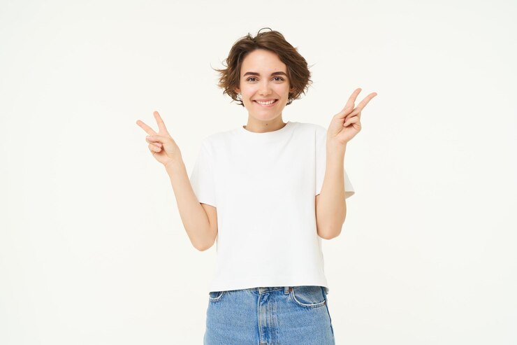 L'immagine di una giovane donna felice e positiva mostra gesti di pace e sorride in piedi sopra il bianco