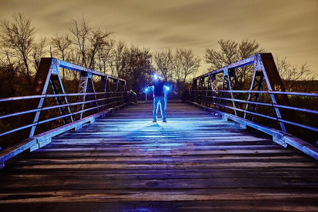 L'immagine di una luce blu brillante circonda un uomo nel mezzo di un ponte di metallo al crepuscolo