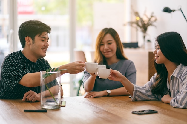 L'immagine ravvicinata di tre persone asiatiche si è divertita a bere e tintinnare le tazze di caffè sul tavolo di legno al bar