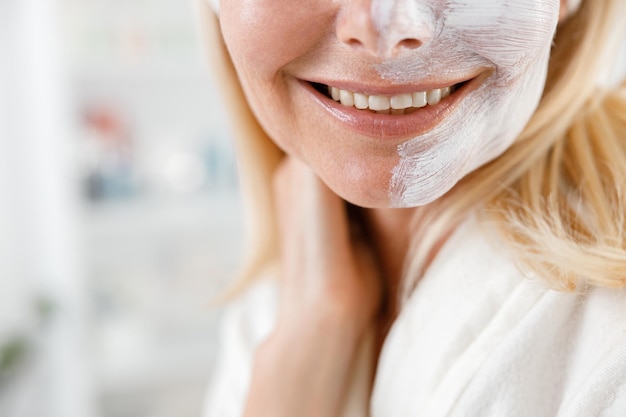 L'immagine ravvicinata di una donna irriconoscibile con una maschera crema bianca su metà del viso sorride