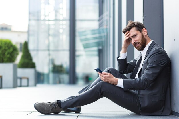 L'impiegato seduto vicino all'ufficio all'aperto ha ricevuto cattive notizie, depresso e stanco legge cattive notizie dal telefono online