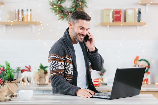 L'imprenditore freelance felice e di successo che lavora al laptop a casa parlando al telefono durante le vacanze di Capodanno completa il progetto entro la scadenza