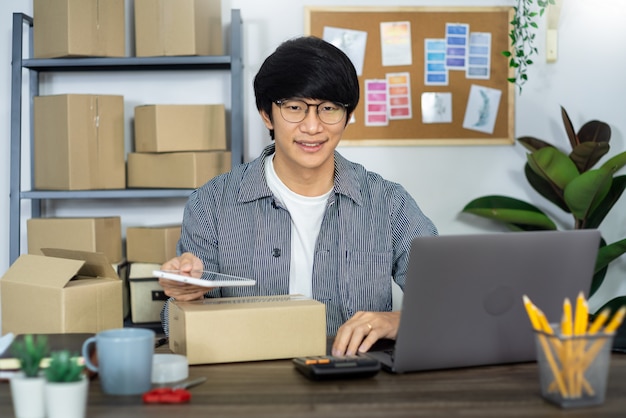 L'imprenditore o startup indipendente asiatico della PMI dell'uomo d'affari che lavora in una scatola di cartone prepara la scatola di consegna per il concetto del cliente, di vendita online, di commercio elettronico, di imballaggio e di spedizione.