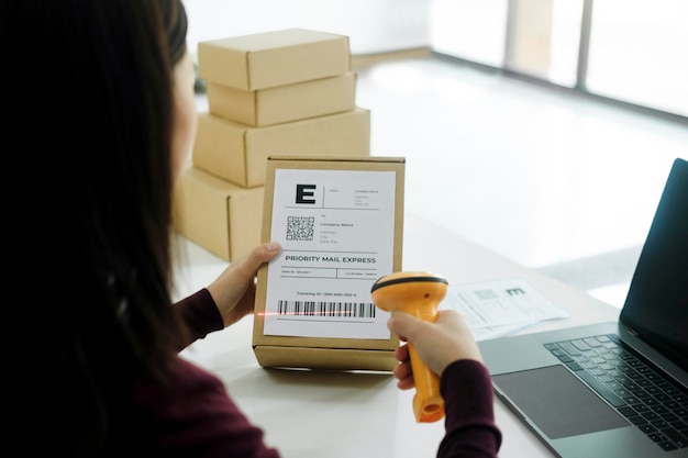 L'imprenditore online femminile esegue la scansione dell'etichetta di spedizione sul pacco