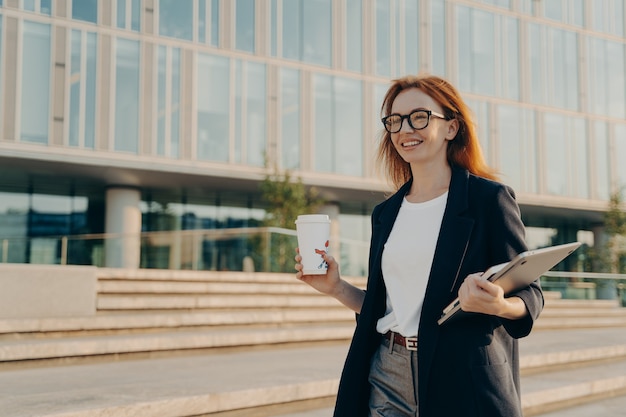 L'imprenditrice di successo beve caffè da asporto trasporta notebook e laptop