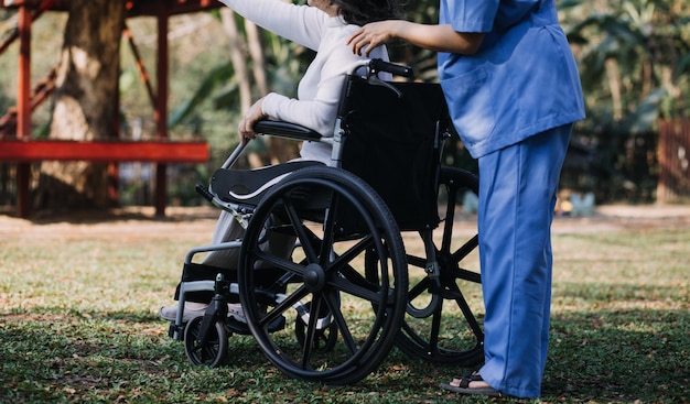 L'infermiera asiatica della giovane donna alla casa di cura si prende cura dell'uomo anziano disabile Il medico del caregiver serve la terapia fisica per il paziente anziano più anziano per esercitarsi e esercitarsi a camminare sul deambulatore o sul bastone nel cortile