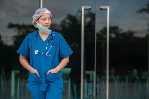 L'infermiera asiatica stanca e depressa indossa l'uniforme blu con maschera facciale seduta sul pavimento dell'ospedale. Giovane dottoressa stressata dal duro lavoro