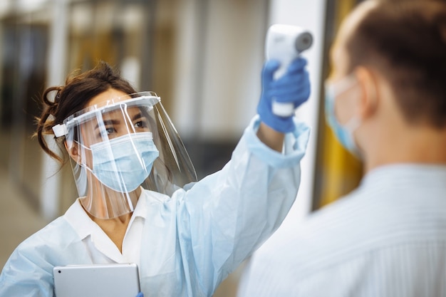 L'infermiera misura la temperatura di un paziente in ospedale con un termometro senza contatto. Persone che indossano maschere mediche protettive. Prevenzione del coronavirus e concetto di assistenza sanitaria.