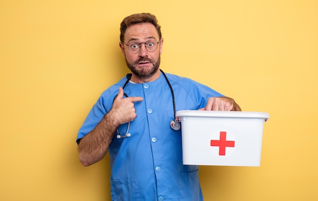 L'infermiera o il medico si sentono felici e puntano a se stessi con un concetto di kit di pronto soccorso eccitato per affari e telefono