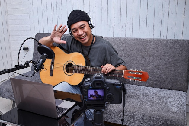 L'influencer asiatico saluta mentre suona la chitarra durante il podcast o la trasmissione video in diretta per il pubblico