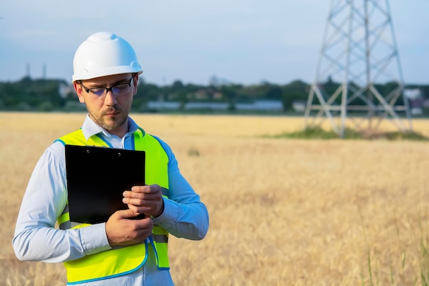 L'ingegnere maschio con casco e occhiali usa uno smartphone per il lavoro sul campo vicino a un rimorchio per telecomunicazioni