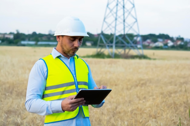 L'ingegnere maschio con casco e occhiali usa uno smartphone per il lavoro sul campo vicino a un rimorchio per telecomunicazioni