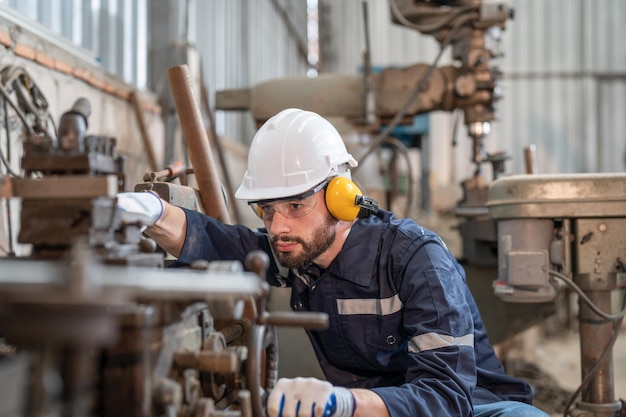 L'ingegnere maschio indossa occhiali protettivi per la protezione dell'udito e casco che lavora con la macchina in fabbrica