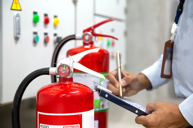 L'ingegnere sta controllando e ispezionando un estintore rosso nella sala controllo antincendio per la prevenzione della sicurezza e l'addestramento antincendio.