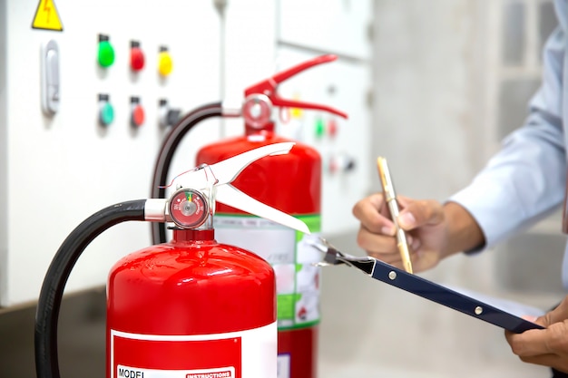 L'ingegnere sta controllando e ispezionando un estintore rosso nella sala di controllo antincendio per sicurezza.