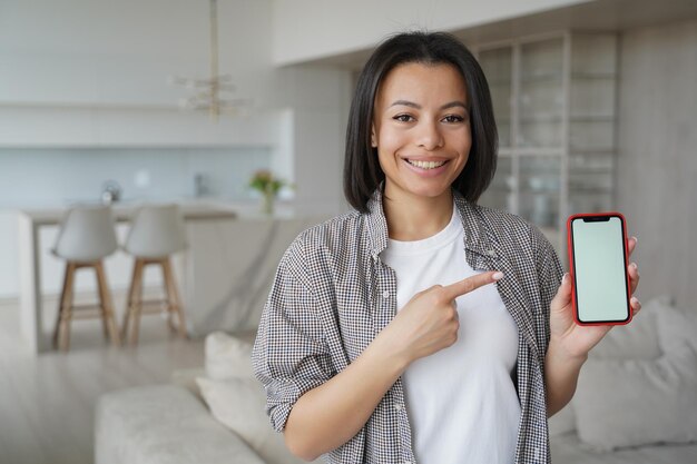 L'inquilino femminile che punta allo smartphone con lo schermo vuoto del mockup consiglia l'app di caccia alla casa a casa