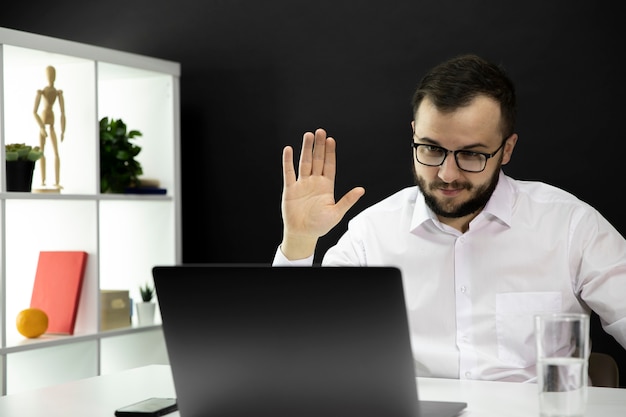 L'insegnante bello tiene la videoconferenza sul computer portatile, mano sollevata nel saluto