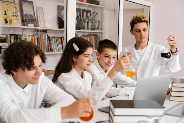 L'insegnante di chimica della scuola mostra ai bambini boccette con liquidi per esperimenti in laboratorio Concetto di istruzione Lezione di gruppo di compagni di classe alla lezione di chimica