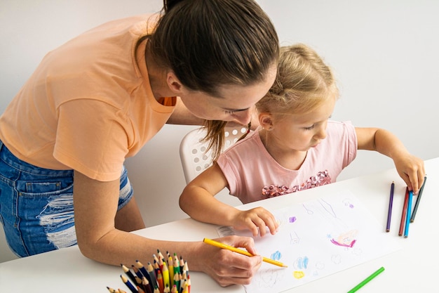 L'insegnante di disegno aiuta la bambina a disegnare con matite colorate su carta