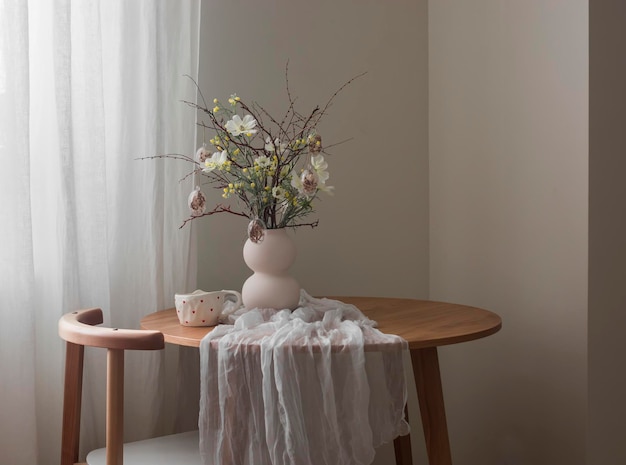 L'interno accogliente del soggiorno un tavolo rotondo con fiori di Pasqua in un vaso di ceramica e una tazza