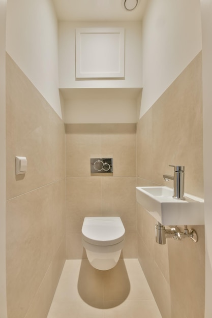 L'interno di un bagno rivestito con piastrelle beige in una casa accogliente con lavabo in ceramica e wc ribaltabile