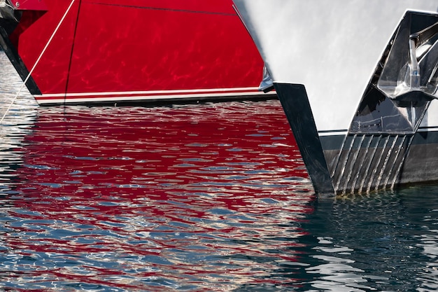 L'ipnotizzante riflesso dell'acqua sul lato lucido di un enorme yacht ancorato con dettagli cromati c...